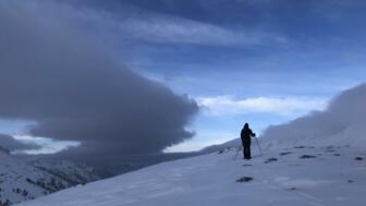 Splitboarder im Aufstieg vor seitlicher Wolkenfront und blauem Himmel.