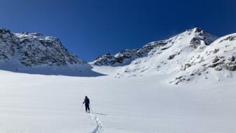 Skitourengeherin im unverspurten Hang im Aufstieg bei Sonne