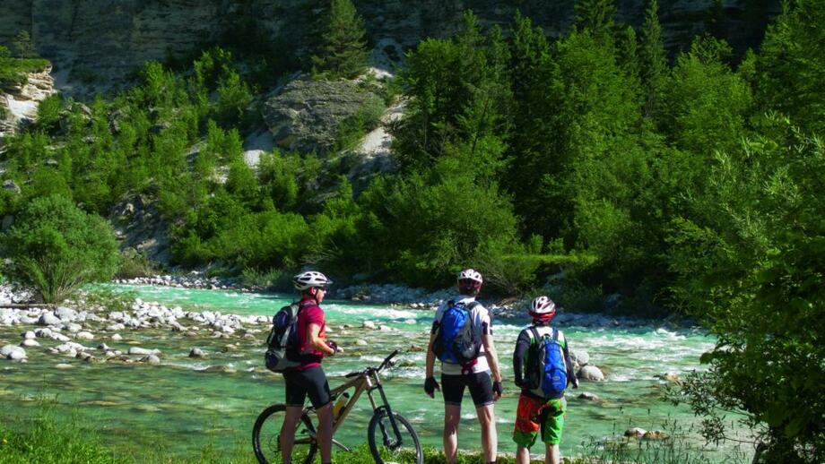 Drei Mountainbiker am türkisklaren Fluss während der Trans Slovenia I.