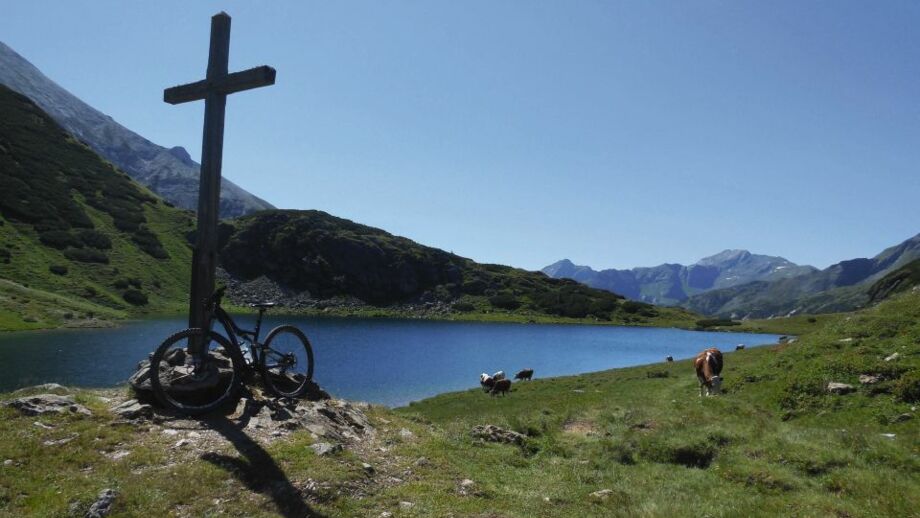 Ein Gipfelkreuz mit See in Hintergrund am Alpenhauptkamm