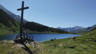 Ein Gipfelkreuz mit See in Hintergrund am Alpenhauptkamm