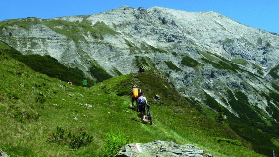 Zwei Mountainbiker*innen auf einem Trail mit den Nockbergen.