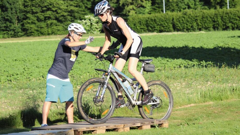 Zwei Mountainbiker*innen beim Üben der Fahrtechniktraining auf einem Hindernis.