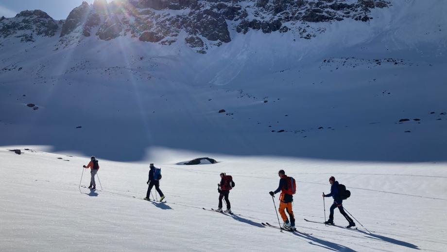 Skitourengruppe auf dem Weg zum Gipfel mit Sonne im Hintergrund und blauem Himmel