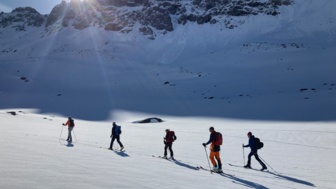 Skitourengruppe auf dem Weg zum Gipfel mit Sonne im Hintergrund und blauem Himmel