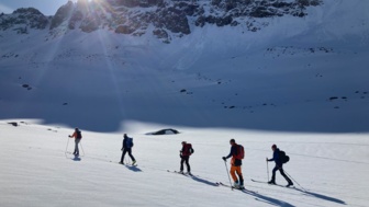 Skitourengruppe auf dem Weg zum Gipfel mit Sonne im Hintergrund und blauem Himmel