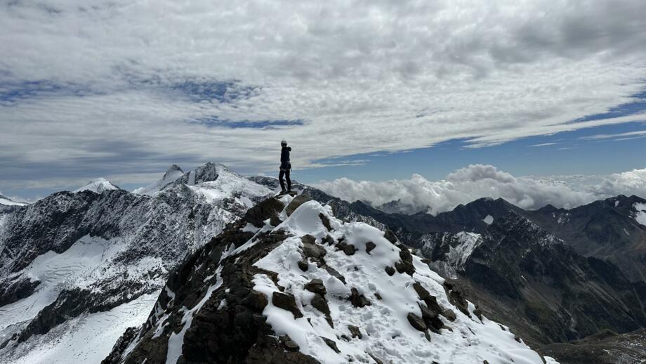 Bergsteigerin auf Gipfel mit Bergpanorama und Wolkenspiel