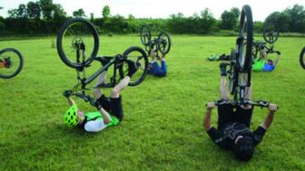 Mountainbiker*innen auf dem Rücken bei Fahrtechnik-Training auf der Wiese