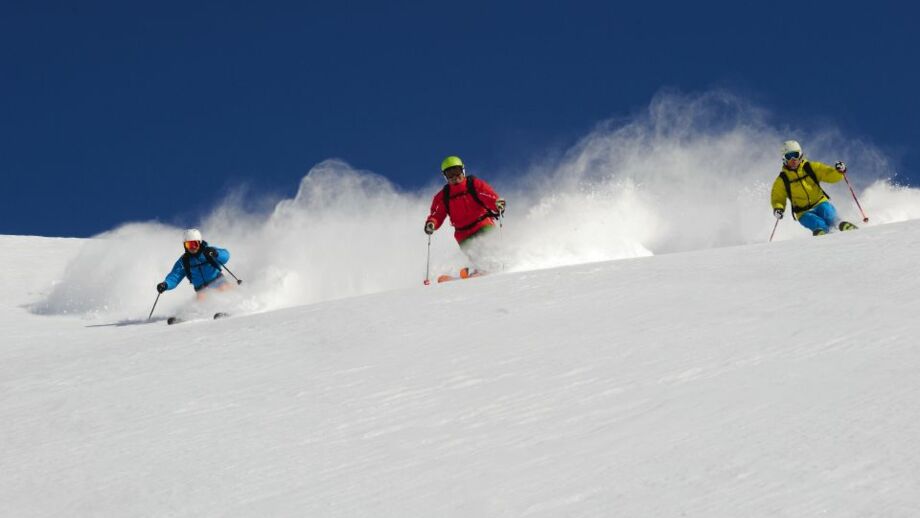 Zwei Skifahrerbei der Tiefschneeabfahrt bei blauem Himmel
