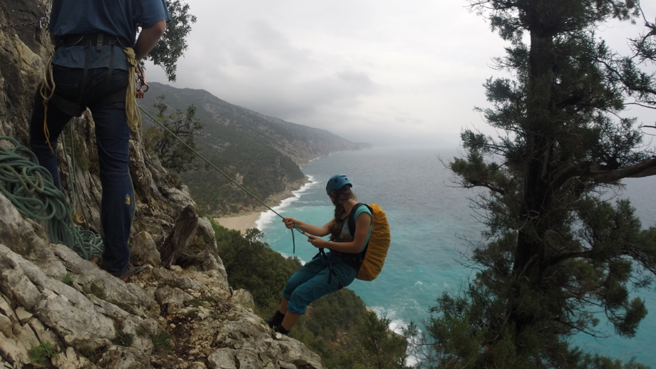 Kletterer hängend am Seil mit Sicherheitsgurten an der Klippe und im Hintergrund der fantastische Sandstrand und das Meer