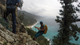 Kletterer hängend am Seil mit Sicherheitsgurten an der Klippe und im Hintergrund der fantastische Sandstrand und das Meer