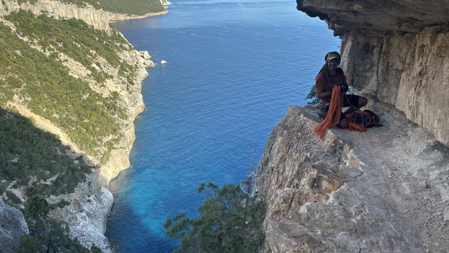 Wanderer an einer sehr steilen Klippe mit Seilen un d im Hintergrund das blaue Meer