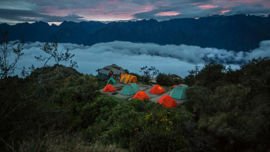 Buntes Zeltlage in der Dämmerung auf einer Anhöhe über Nebelschwaden in der Cordillera Urubamba