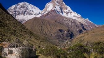 Rundbauten vor mächtiger Bergkulisse in Peru