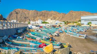 Bunte Fischerboote an der Küste des Oman vor Felslandschaft