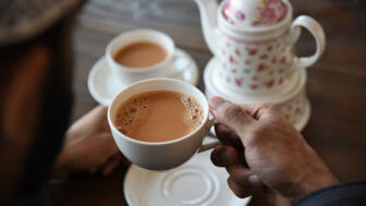 Hand hält Teetasse und weiteres Teegeschirr