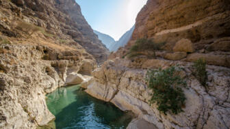 Fluss, Felsen und einzelne grüne Sträucher im Wadi Shaab im Oman