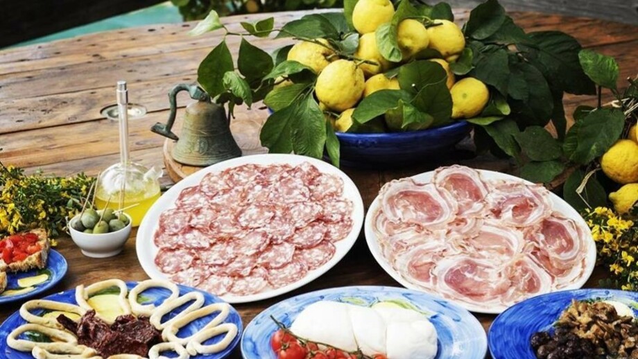 Servierplatten auf einem Holztisch, eine Schüssel Zitronen, Salami, Speck, Käse, Oliven und TOmete Mozarella