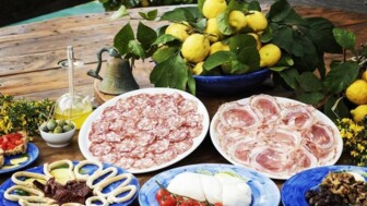 Servierplatten auf einem Holztisch, eine Schüssel Zitronen, Salami, Speck, Käse, Oliven und TOmete Mozarella