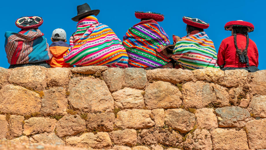 Vier einheimische mit traditioneller Kleidung die auf einer Mauer sitzen, Aufnahme von Hinten