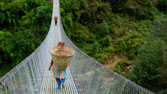 nepal-hilha-nepalese-woman-carrying-a-wicker-basket-on-her-back-walking-on-a-hanging-bridge-during-trekking-on-trail-from-ghangaruk-to-phedi-shutterstock_1597712782.jpg