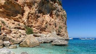 Küsten Aufnahme von einer Klippe mit wundervollem türkis blauem Meerblick und Booten im Hintergrund in Cala Biriala