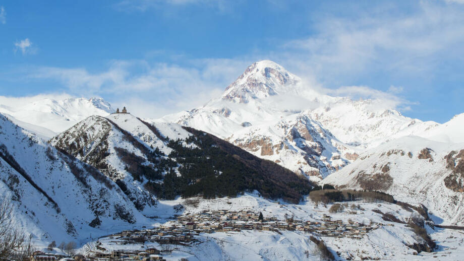 Tief verschneite Winerlandschaftg mit Ort stepantsminda, Dreifaltigkeitskirche Gergeti und dem Fünftausender Kasbek in Georgien