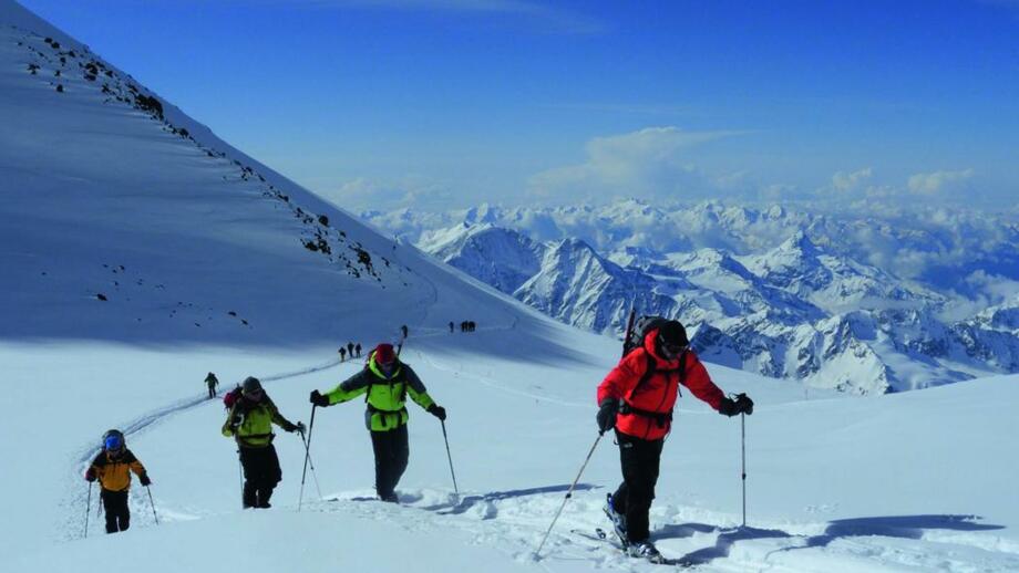 Gruppe von Skibergsteigern im winterlichen Aufstieg zum Fünftausender Kasbek mit Blick auf weitere schneebedeckte Kaukasus-Gipfel