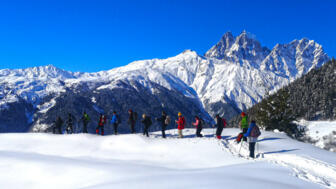 Eine große Gruppe an Schneeschuhwanderern auf verschneiten Wegen