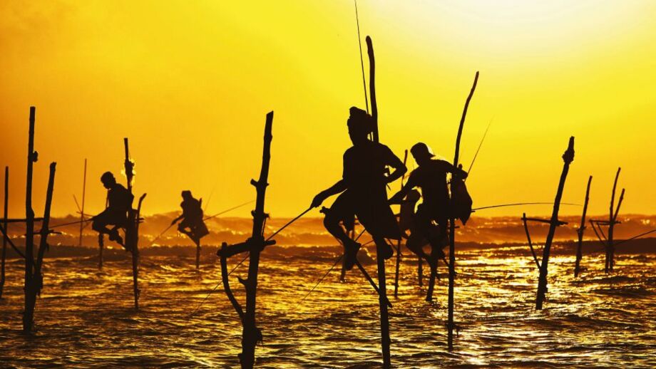 Vier Fischer sietzen bei Sonnenuntergang auf Pfählen im Meer nahe Galle und es sind nur schattige Umrisse zu erkennen