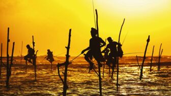 Vier Fischer sietzen bei Sonnenuntergang auf Pfählen im Meer nahe Galle und es sind nur schattige Umrisse zu erkennen