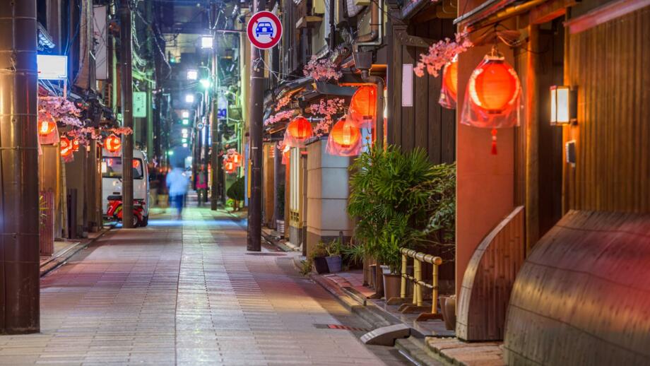 Nächtliche Stassenszene in Kyoto mit Spaziergänger und range und rrot erleuchteten Lampions