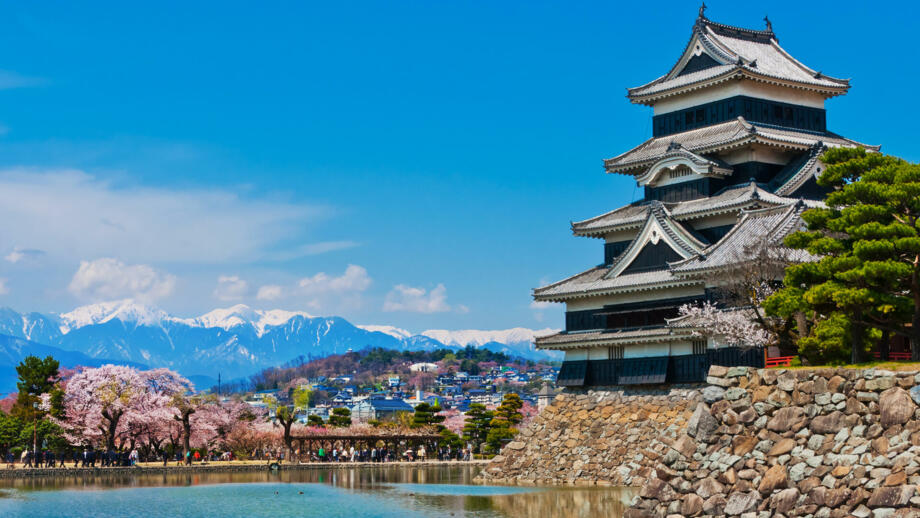 Pagodenähnliche Krähenburg in Matsumoto mit Blick auf Fluss, blühende Kirschbäume, Stadt und Gebirge