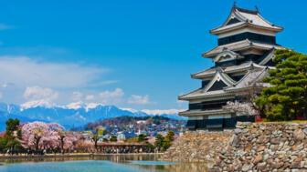 Pagodenähnliche Krähenburg in Matsumoto mit Blick auf Fluss, blühende Kirschbäume, Stadt und Gebirge