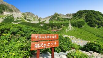 Willkommensschild der Karasawa-Hütte im Chubu-Sangaku-Nationalpark in den Japanischen Alpen, grüne Gebirgdslandschaft mit feslsigen Bergen