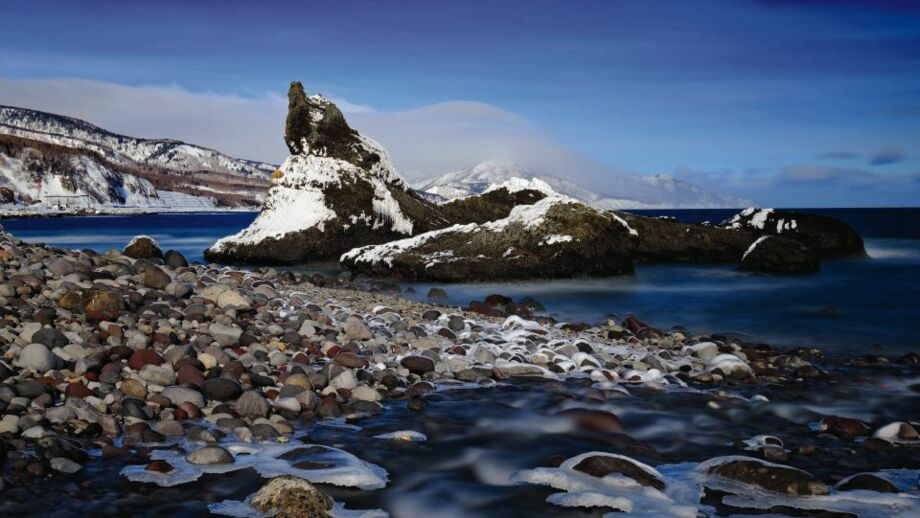Küste des Ochotskischen meeres mit Felsen, Kieseln und etwas schnee auf der Insel Hokkaido