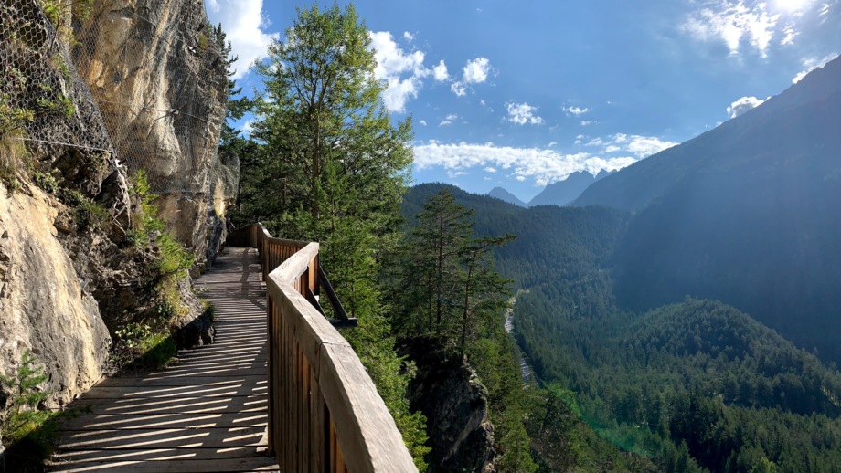 Eine Brücke am Gardasee. Im Hintergrund ist die Bergwelt der Gardaseeberge zu sehen. Die Sonne scheint. Der Himmel ist leicht bewölkt.
