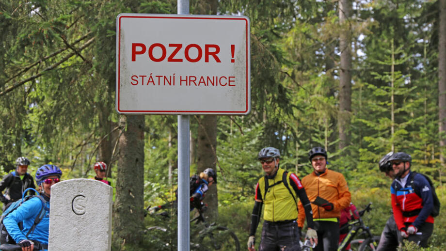 Eine Mountainbike Gruppe im Wald. Sie sind am Grenzübergang zu Tschechien. Das Grenzschild mit dem Wort Pozor steht in der Mitte.