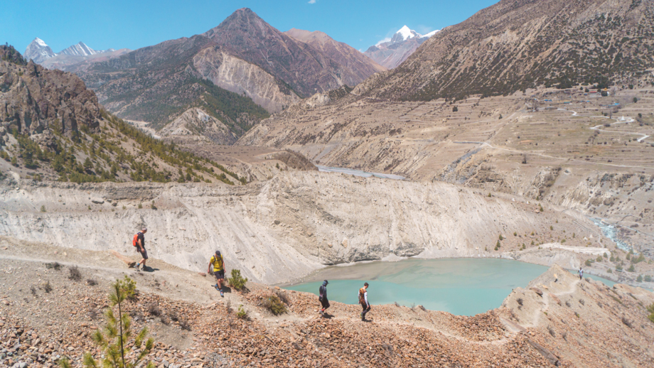 Eine Mountainbike Gruppe während einer Wanderung zur Akklimatiersierung. Ein See und das Annapurnagebirge im Hintergrund.