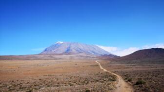 Der Kilimandscharo im Hintergrund. Im Vordergrund ist die Sandpiste der Mountainbikebesteigung Kilimandscharo zu sehen.