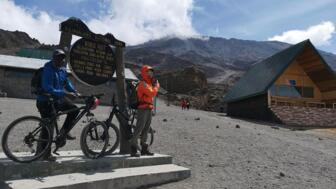 Eine Gruppe von Mountainbiker auf Ihrem Weg zum Gipfel des Kilimandscharos. Sie stehen am Schild der Kibo-Hütte. Ein Zwischenziel.