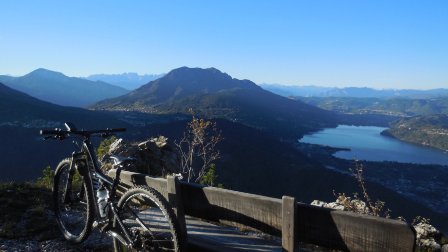 Ein Mountainbike an einen Zaun angelegt mit Ausblick auf die umliegende Bergwelt und den See.