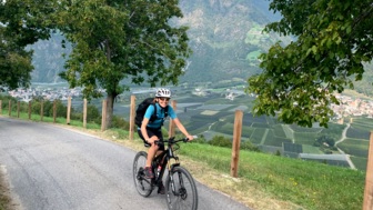 Eine Mountainbikerin fährt auf einer Asphaltstrasse. Im Hintergrund sind die Berge zu sehen.