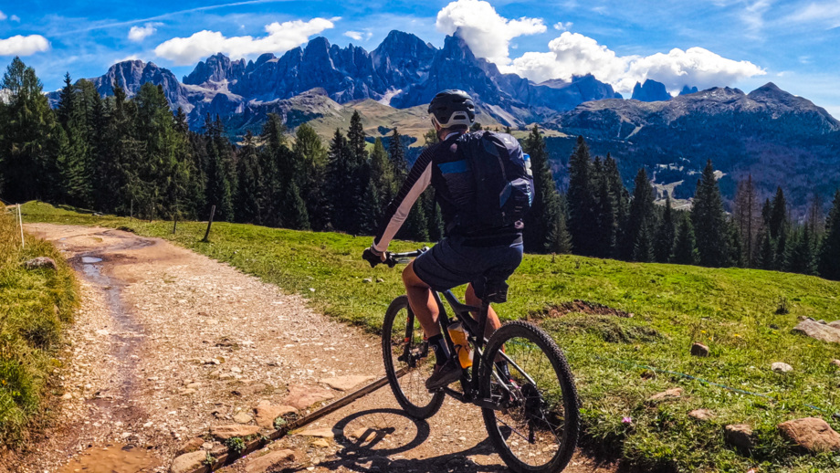 Eine Moutainbikerin fährt auf einer Forststrasse. Im Hintergrund sind die Dolomiten zu sehen.