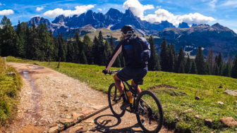 Eine Moutainbikerin fährt auf einer Forststrasse. Im Hintergrund sind die Dolomiten zu sehen.