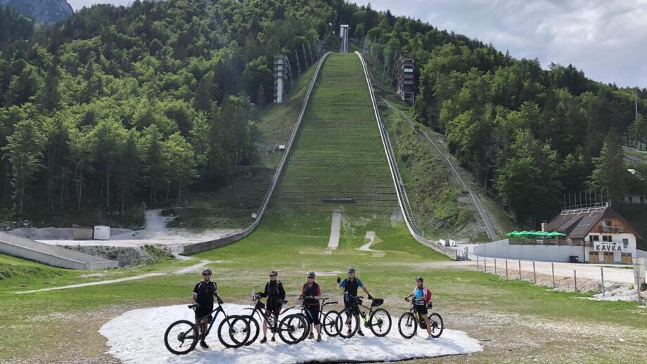 Eine Gruppe an Mountainbiker steht vor eine Skisprungschanze.