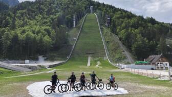 Eine Gruppe an Mountainbiker steht vor eine Skisprungschanze.