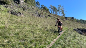 Eine Mountainbikerin auf einem Trail im Altmühltal. Die Landschaft ist eine Wiesenlandschaft. Die Sonne scheint.
