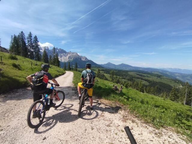 Zwei Mountainbiker mit dem Krücken auf Ihrem Moutainbike auf einer Forststraße. Die Berge im Hintergrund.