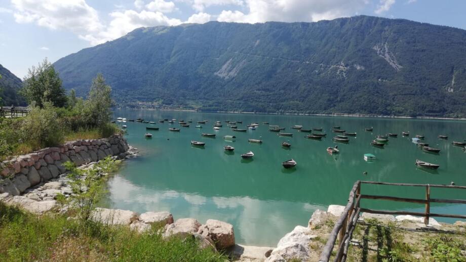 Ein See unterweges auf dem Weg der Crossbike Transalp von München nach Venedig.  Die Berge sind im Hintergrund. Die Sonne scheint.